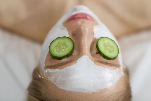 Bella giovane donna che riceve maschera facciale di cetriolo nel salone di bellezza — Foto Stock