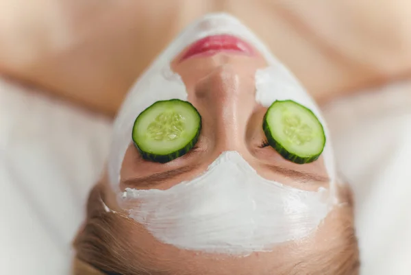 Gyönyörű fiatal nő kap arc maszk uborka szépségszalonban — Stock Fotó