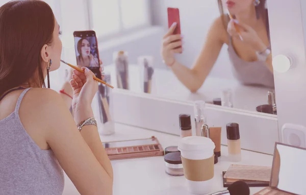 Blogger de belleza filmando tutorial de maquillaje con teléfono inteligente frente al espejo —  Fotos de Stock