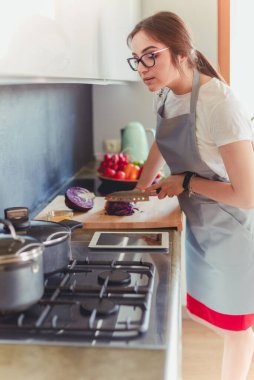 Mutfakta yemek yapmak için tablet bilgisayar kullanan genç bir kadın.