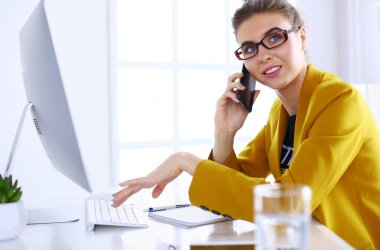 İş kadını ofiste bilgisayar ve cep telefonu kullanarak işine konsantre oluyor.