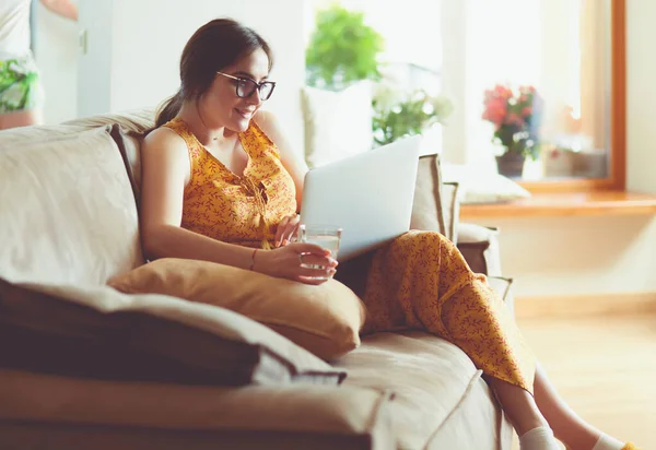 自宅でラップトップコンピュータで作業するソファに座っている若い女性 — ストック写真