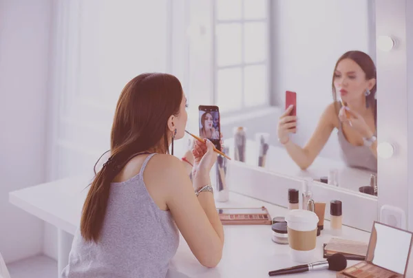 Beauty blogger filming makeup tutorial with smartphone in front of mirror
