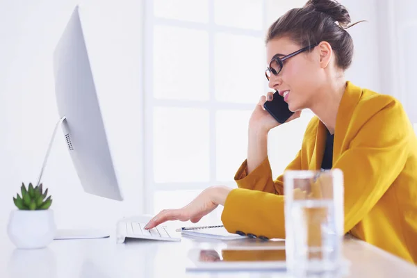 Portrait of beautiful woman making call while sitting at her workplace in front of laptop and working on new project — Stock Photo, Image