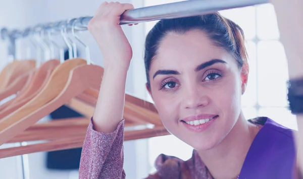 Beautiful young stylist near rack with hangers