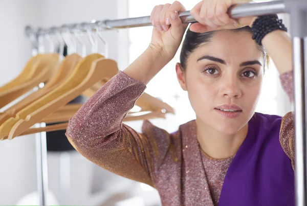 Bonito jovem estilista perto de rack com cabides — Fotografia de Stock