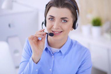 Ofisinde kulaklık takmış, telefon operatörü olarak çalışan ciddi ve güzel bir genç kadın.