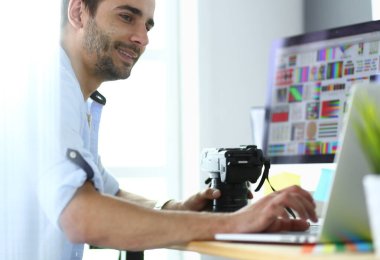 İnternette çalışırken bilgisayarın ve dizüstü bilgisayarın önünde grafik stüdyosunda oturan genç tasarımcının portresi.