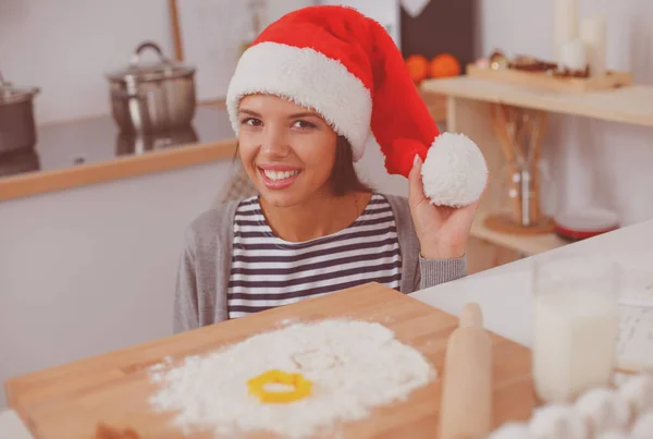 Noel Baba şapkalı kadın mutfakta Noel kurabiyesi yapıyor. — Stok fotoğraf
