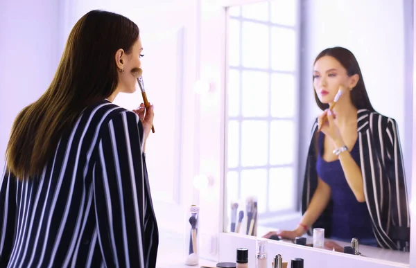 Hermosa chica mirando en el espejo y la aplicación de cosméticos con un cepillo grande — Foto de Stock