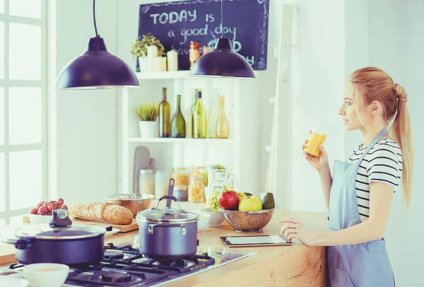Vonzó nő kezében egy pohár narancslé, miközben áll a konyhában — Stock Fotó