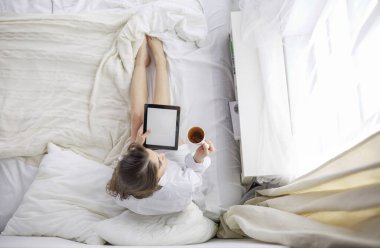 Sabahları yatakta otururken tablet kullanan ve kahve içen kadın portresi