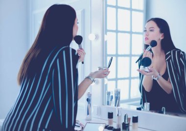 Güzel kız aynaya bakıyor ve büyük bir fırçayla kozmetik uyguluyor.