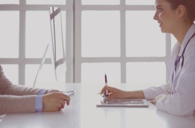 Muayene odasında oturup çalışırken dijital tablet kullanan orta yaşlı kadın doktor portresi