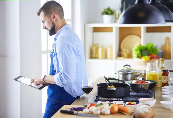 デジタルタブレット上のレシピに従う男と自宅でキッチンでおいしいと健康食品を調理 — ストック写真