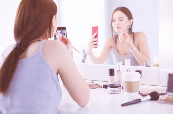 Blogger de belleza filmando tutorial de maquillaje con teléfono inteligente frente al espejo —  Fotos de Stock