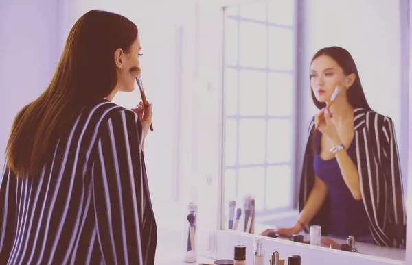 Schönes Mädchen, das in den Spiegel schaut und Kosmetik mit einem großen Pinsel anwendet — Stockfoto