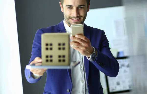 Empresario sosteniendo la casa en miniatura en la mano de pie en la oficina . —  Fotos de Stock