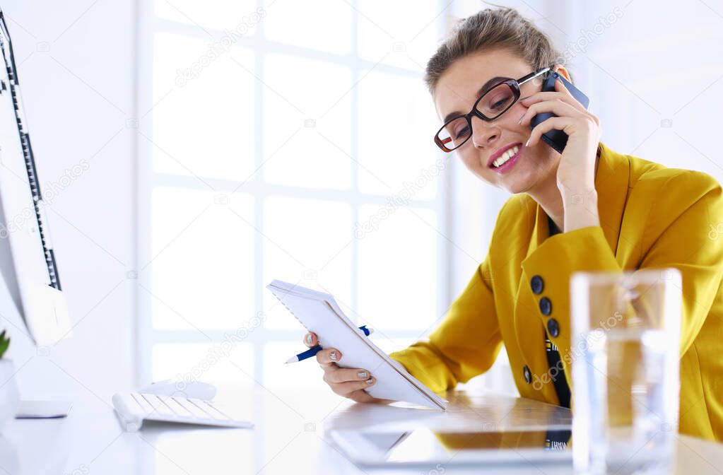 Portrait of beautiful woman making call while sitting at her workplace in front of laptop and working on new project