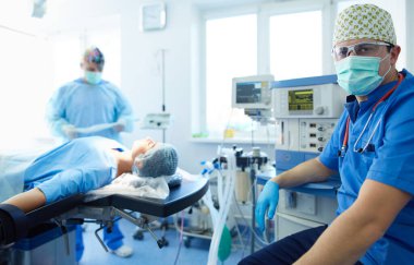 Ameliyat odasında arka planda erkek cerrah var.