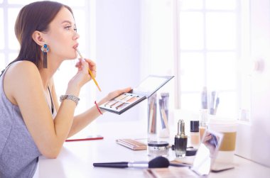 Esmer bir kadın aynanın önünde akşam randevusunu telafi etmek için başvuruyor.