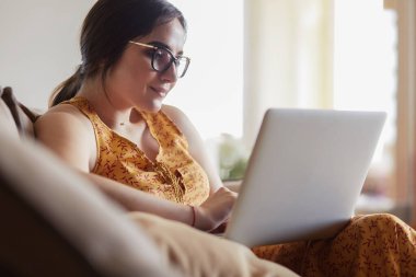 Evde dizüstü bilgisayar üzerinde çalışan kanepede oturan genç kadın