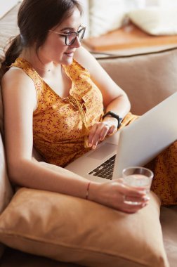 Evde dizüstü bilgisayar üzerinde çalışan kanepede oturan genç kadın