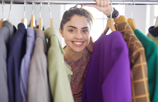 Beautiful young stylist near rack with hangers