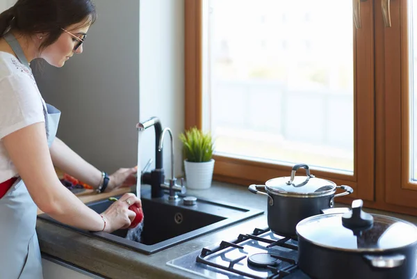 Een vrouw die groenten wast. mooie jonge vrouw wassen groenten voor salade en glimlachen terwijl staan in de keuken — Stockfoto