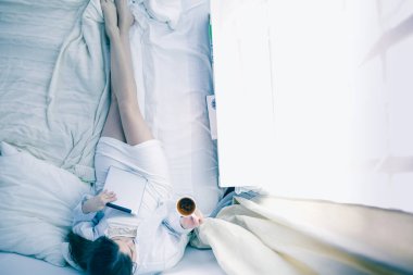 Sabahları yatakta otururken tablet kullanan ve kahve içen kadın portresi