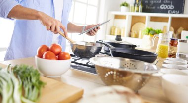 Dijital tablet ve yemek pişirme tarifine uyan bir adam evdeki mutfakta lezzetli ve sağlıklı yemekler pişiriyor.