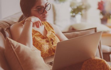 Evde dizüstü bilgisayar üzerinde çalışan kanepede oturan genç kadın