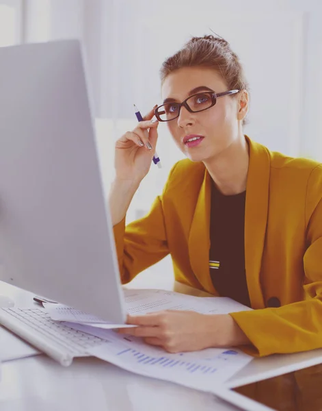 Hermosa joven mujer de negocios haciendo un poco de papeleo mientras está sentado en el escritorio de la oficina delante de la computadora portátil — Foto de Stock