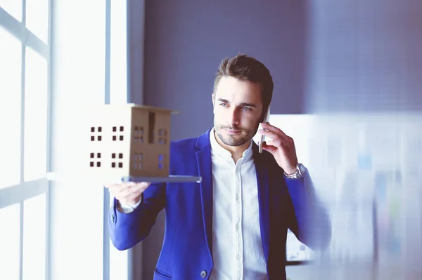 Homme d'affaires tenant maison miniature à portée de main debout dans le bureau . — Photo