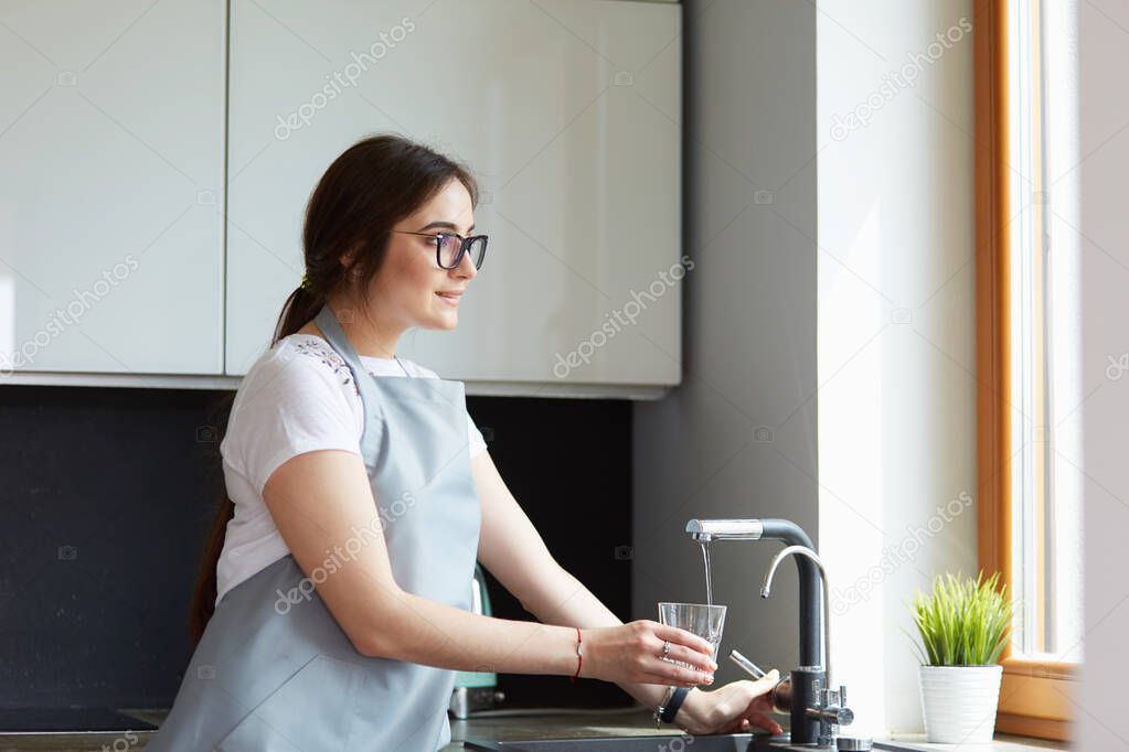 Woman filling a glass of water from a stainless steel or chrome tap or faucet