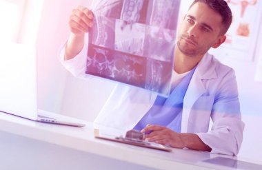 Genç doktor ofisinde oturuyor ve röntgen sonuçlarını inceliyor.