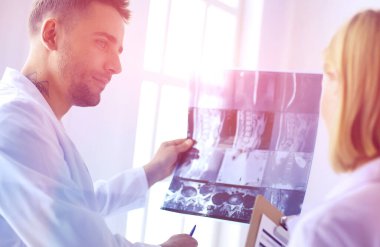 Yakışıklı doktor genç bayan hastasıyla konuşuyor ve ofisinde otururken notlar alıyor.