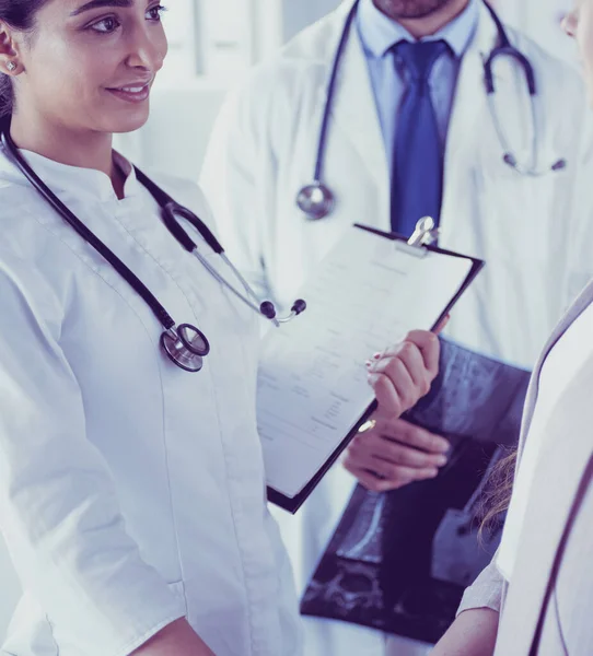 Médico bonito está conversando com jovem paciente do sexo feminino e fazendo anotações enquanto está sentado em seu escritório — Fotografia de Stock