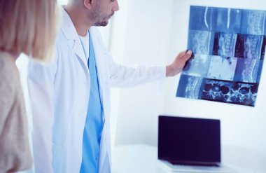 Yakışıklı doktor genç bayan hastasıyla konuşuyor ve ofisinde otururken notlar alıyor.