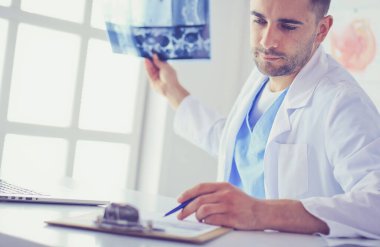 Genç doktor ofisinde oturuyor ve röntgen sonuçlarını inceliyor.