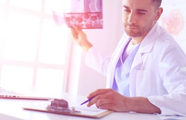 Genç doktor ofisinde oturuyor ve röntgen sonuçlarını inceliyor.