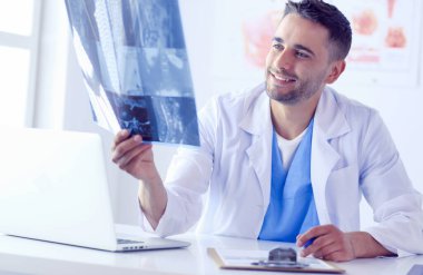 Genç doktor ofisinde oturuyor ve röntgen sonuçlarını inceliyor.