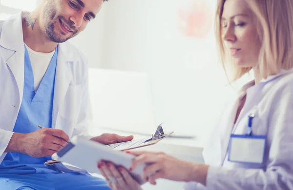 Knappe dokter praat met jonge vrouwelijke patiënt en maakt aantekeningen terwijl hij in zijn kantoor zit — Stockfoto