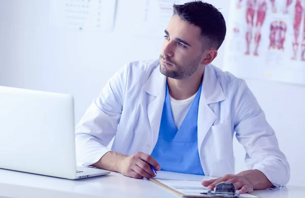 Ritratto di un medico di sesso maschile con computer portatile seduto alla scrivania nello studio medico — Foto Stock