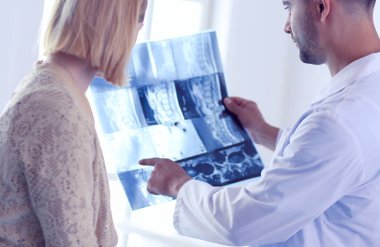 Yakışıklı doktor genç bayan hastasıyla konuşuyor ve ofisinde otururken notlar alıyor..