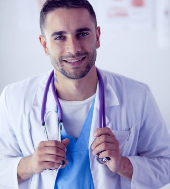 Genç ve kendinden emin erkek doktor portresi tıp ofisinde duruyor..