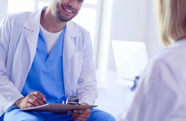 Schöner Arzt spricht mit junger Patientin und macht sich Notizen, während er in seinem Büro sitzt — Stockfoto