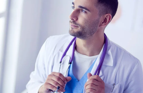 Retrato médico masculino joven y confiado de pie en el consultorio médico. —  Fotos de Stock