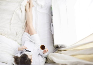 Sabahları yatakta otururken tablet kullanan ve kahve içen kadın portresi