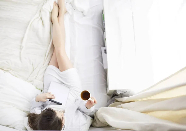 Портрет женщины с помощью планшета и пить кофе, сидя на кровати утром — стоковое фото